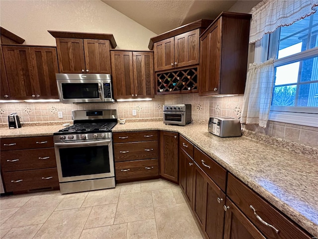 kitchen with vaulted ceiling, appliances with stainless steel finishes, light tile patterned flooring, tasteful backsplash, and light stone countertops