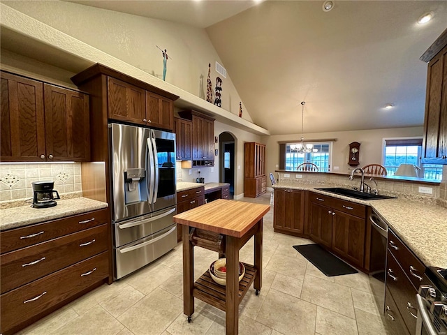 kitchen with sink, hanging light fixtures, stainless steel appliances, light stone counters, and tasteful backsplash