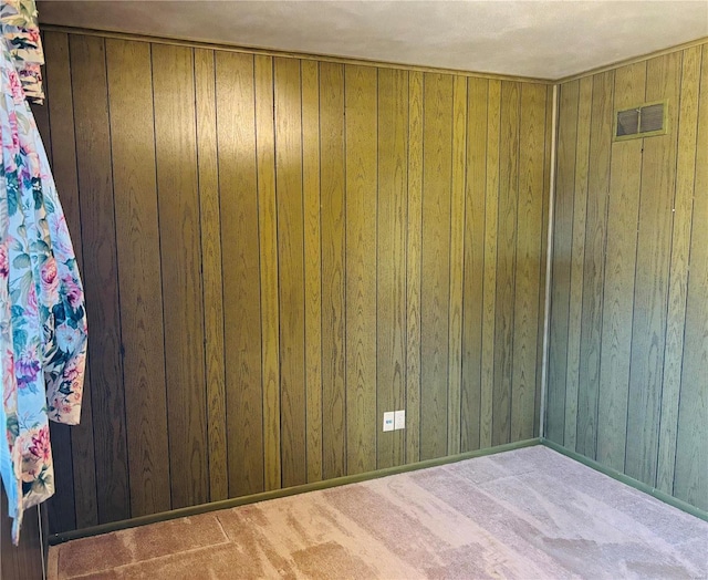 carpeted spare room featuring wood walls and visible vents