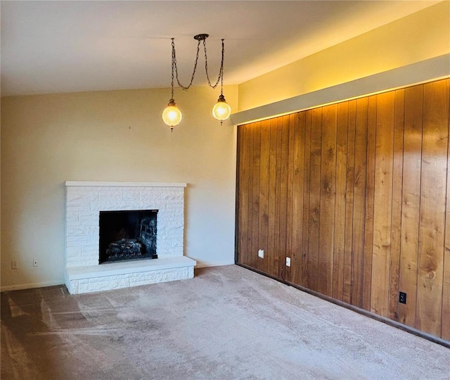 unfurnished living room with carpet floors, wooden walls, a fireplace with raised hearth, and lofted ceiling