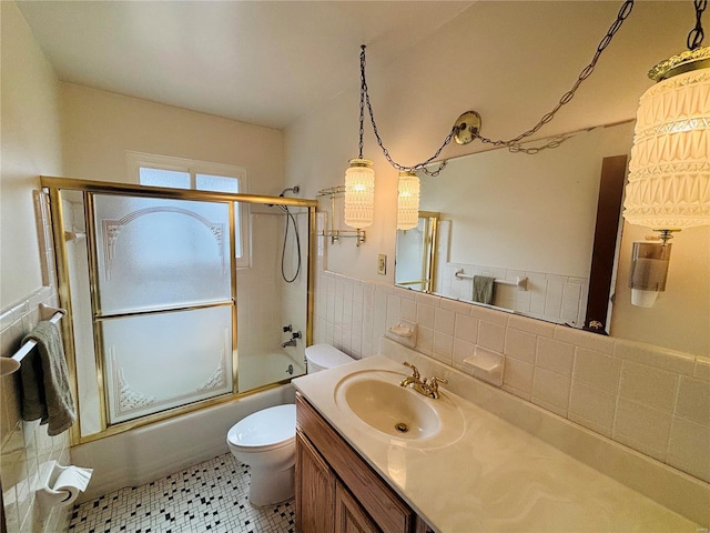 bathroom with bath / shower combo with glass door, wainscoting, toilet, vanity, and tile walls