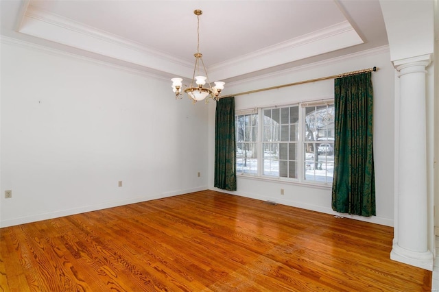 unfurnished room featuring decorative columns, wood-type flooring, a tray ceiling, and ornamental molding