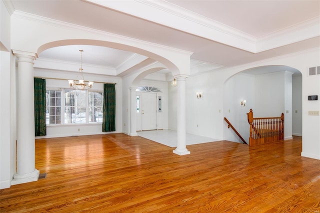 foyer entrance with a notable chandelier, ornate columns, wood-type flooring, ornamental molding, and a tray ceiling