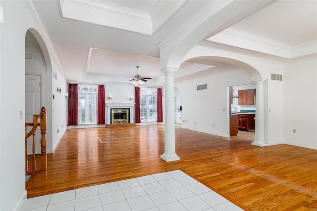 unfurnished living room featuring ornate columns, light tile patterned floors, ornamental molding, ceiling fan, and a tray ceiling