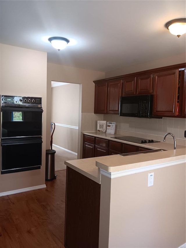 kitchen featuring dark brown cabinetry, dark hardwood / wood-style flooring, kitchen peninsula, and black appliances