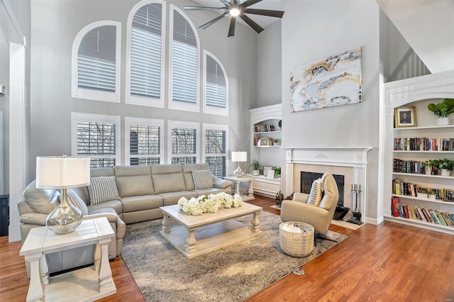 living room featuring a high ceiling, wood-type flooring, ceiling fan, and built in shelves