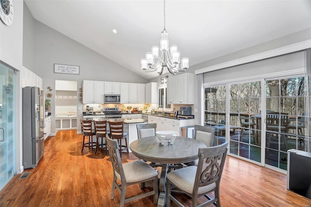 dining room featuring high vaulted ceiling, a chandelier, sink, and light wood-type flooring