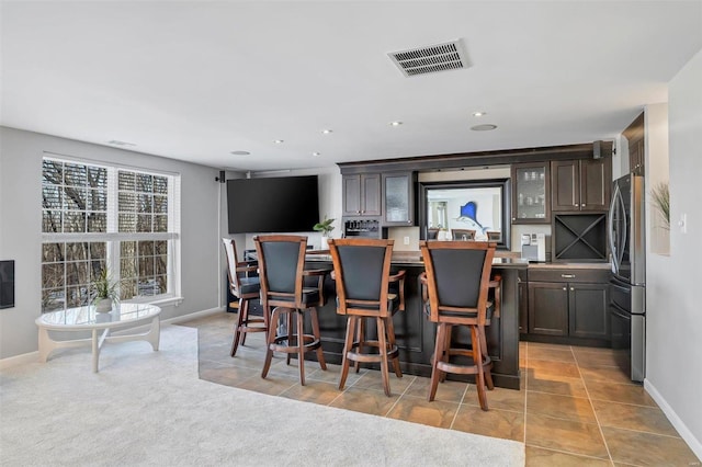 bar with dark brown cabinetry, stainless steel fridge, and light tile patterned flooring