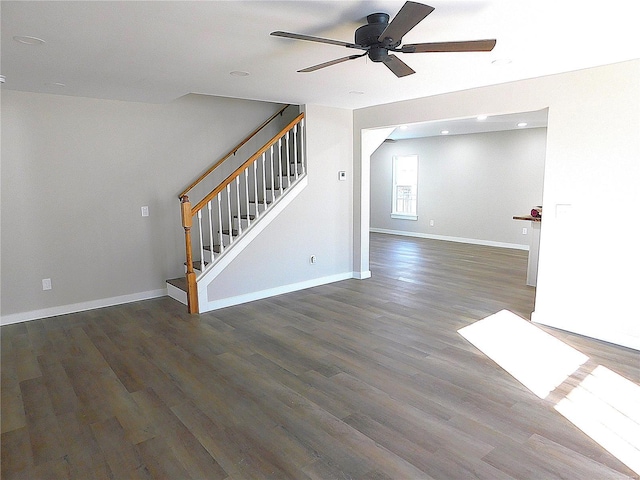 unfurnished living room featuring a ceiling fan, baseboards, stairway, and wood finished floors