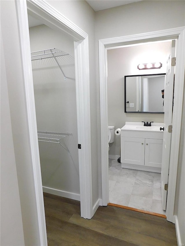 bathroom featuring toilet, a spacious closet, vanity, and wood finished floors