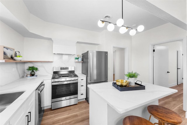 kitchen featuring decorative light fixtures, a breakfast bar area, white cabinets, stainless steel appliances, and light hardwood / wood-style flooring