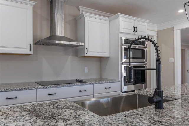 kitchen featuring wall chimney range hood, crown molding, white cabinetry, double oven, and black electric stovetop