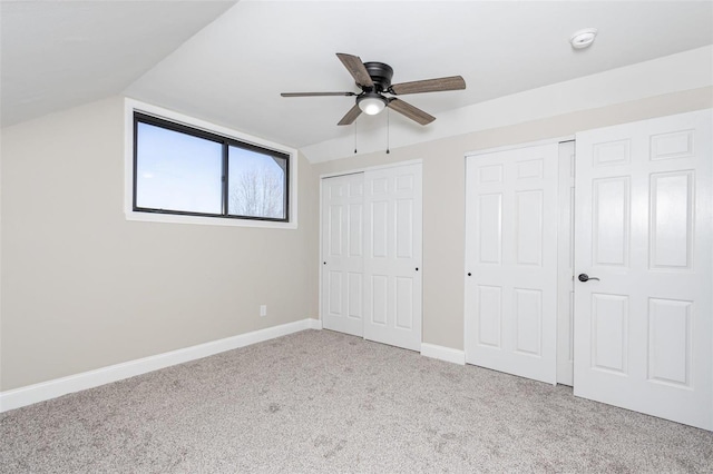 unfurnished bedroom with ceiling fan, light colored carpet, lofted ceiling, and two closets