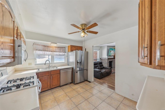 kitchen with light tile patterned flooring, sink, ceiling fan, stainless steel appliances, and a fireplace