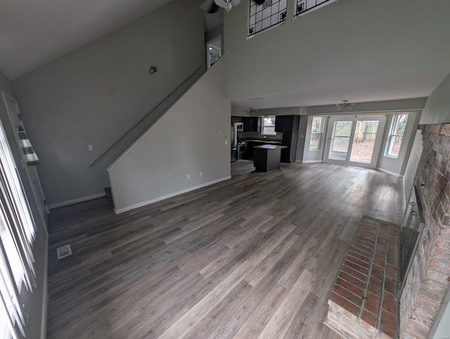 unfurnished living room featuring ceiling fan, a towering ceiling, dark hardwood / wood-style floors, and a brick fireplace