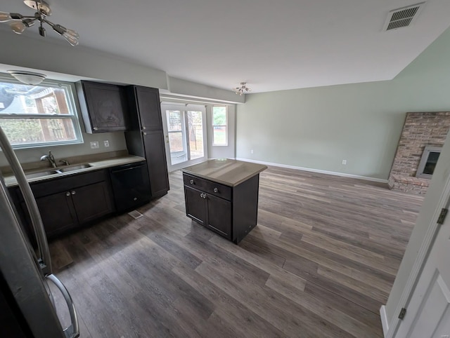 kitchen featuring dishwasher, sink, dark wood-type flooring, a stone fireplace, and a kitchen island