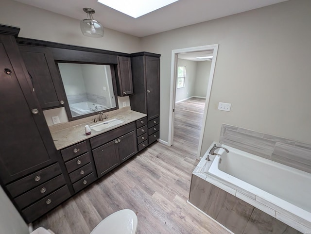 bathroom with hardwood / wood-style flooring, a relaxing tiled tub, vanity, and a skylight