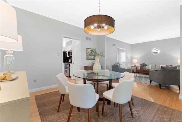 dining area featuring light wood-type flooring, ornamental molding, a notable chandelier, and visible vents