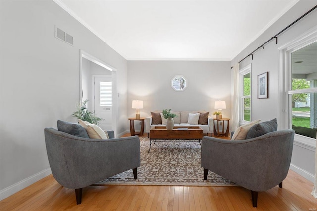 living room with visible vents, ornamental molding, baseboards, and light wood-type flooring