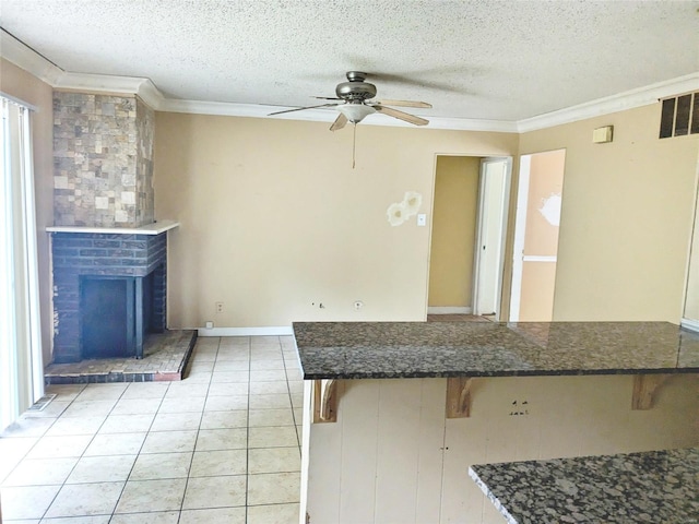 kitchen with a textured ceiling, ceiling fan, light tile patterned floors, crown molding, and a breakfast bar area