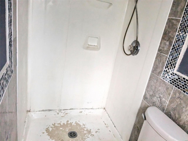 bathroom featuring toilet, a shower, and tile walls