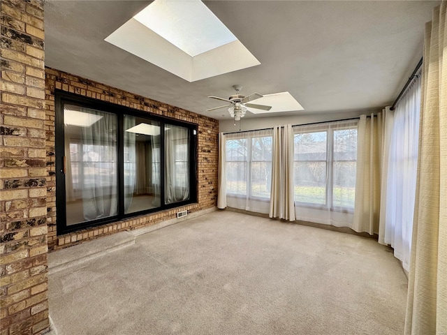 interior space featuring ceiling fan, brick wall, and a skylight