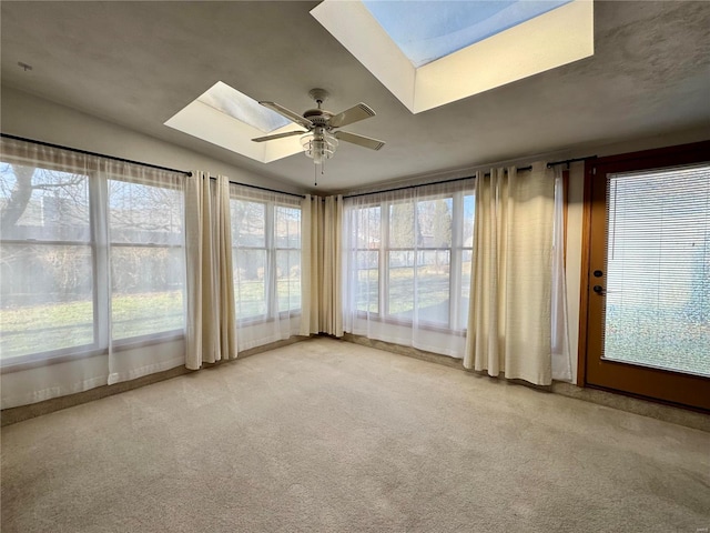 empty room featuring ceiling fan, light colored carpet, and a skylight