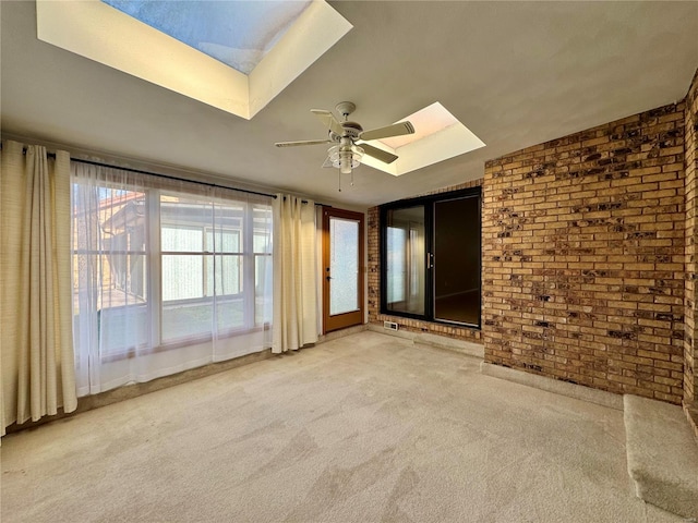 spare room with ceiling fan, brick wall, a skylight, and light carpet