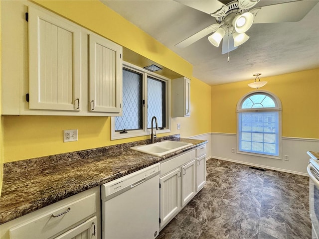 kitchen with sink, white cabinetry, dark stone countertops, white dishwasher, and ceiling fan