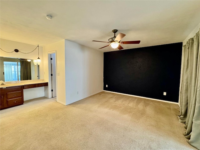 unfurnished bedroom with built in desk, light colored carpet, and ceiling fan