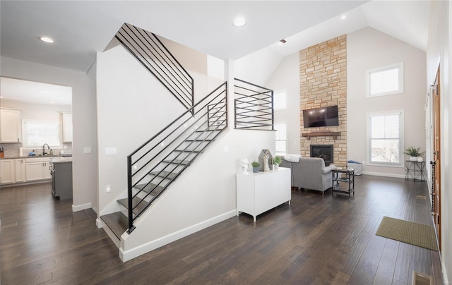 staircase featuring sink, high vaulted ceiling, hardwood / wood-style floors, and a fireplace