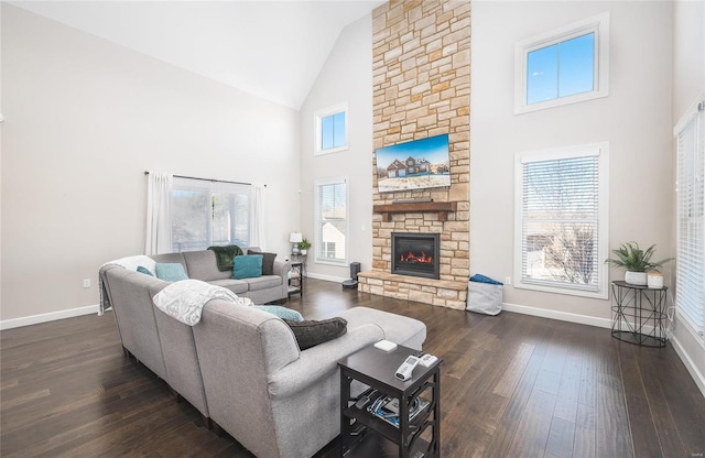 living room with dark wood-type flooring, high vaulted ceiling, a stone fireplace, and a healthy amount of sunlight