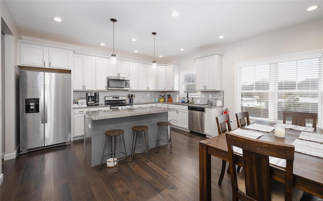 kitchen featuring a center island, appliances with stainless steel finishes, light stone countertops, hanging light fixtures, and white cabinets