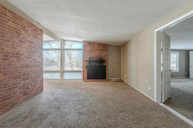 unfurnished living room with a fireplace, lofted ceiling, carpet flooring, and brick wall