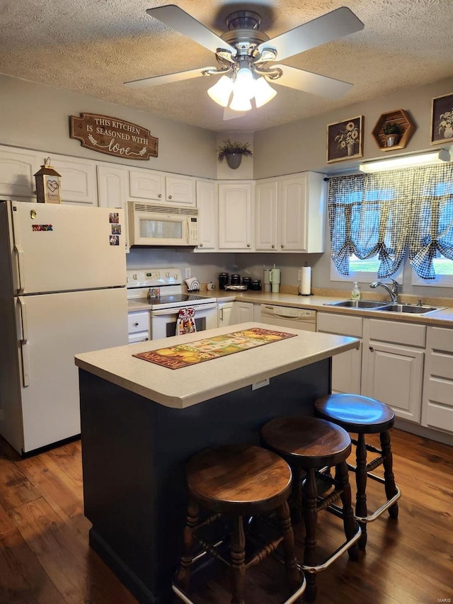 kitchen with a textured ceiling, white cabinetry, a center island, and white appliances