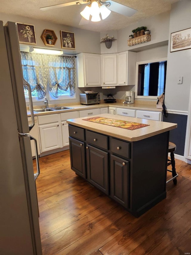 kitchen with a center island, white cabinetry, dark hardwood / wood-style flooring, sink, and fridge