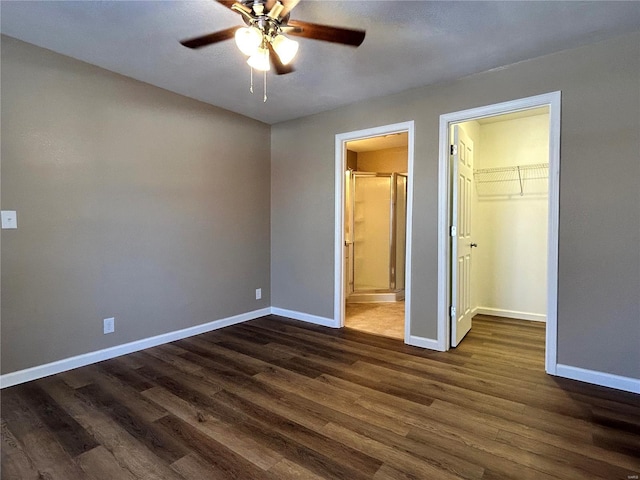 unfurnished bedroom featuring a spacious closet, baseboards, dark wood finished floors, and ensuite bathroom