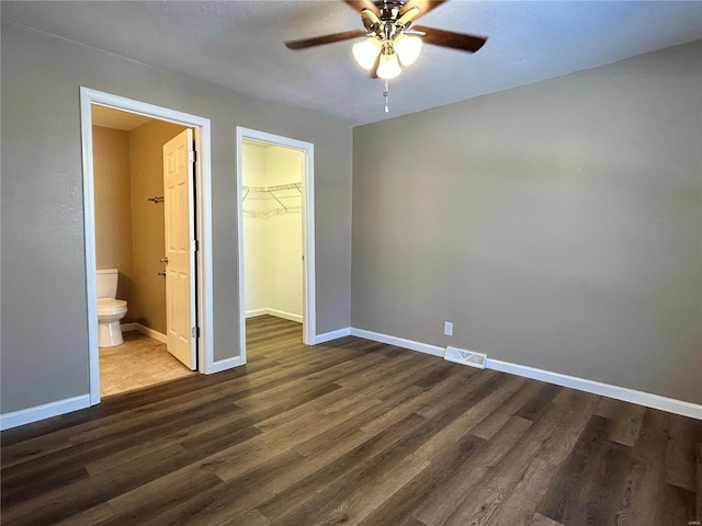 unfurnished bedroom featuring a walk in closet, a closet, visible vents, wood finished floors, and baseboards