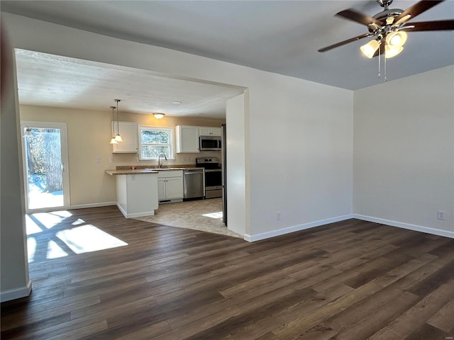 interior space with a ceiling fan, a sink, dark wood finished floors, and baseboards