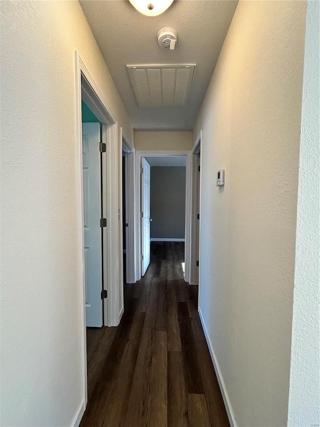 corridor featuring dark wood-type flooring, visible vents, and baseboards