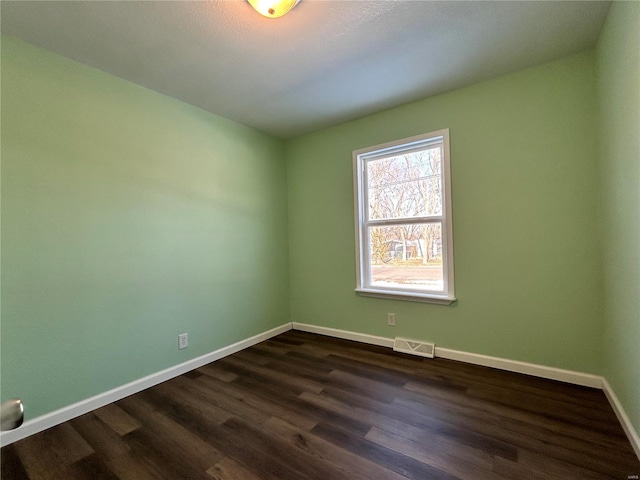 empty room featuring dark wood-type flooring, visible vents, and baseboards