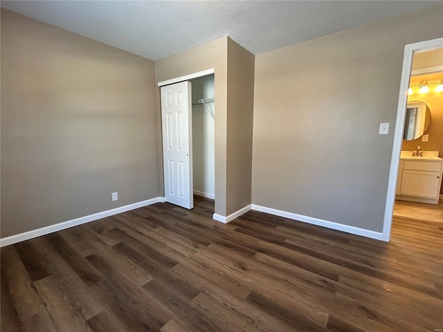 unfurnished bedroom featuring dark wood-style floors, a closet, a sink, and baseboards