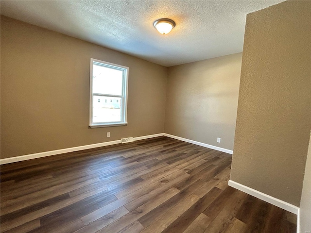 spare room featuring a textured ceiling, dark wood-style flooring, visible vents, and baseboards