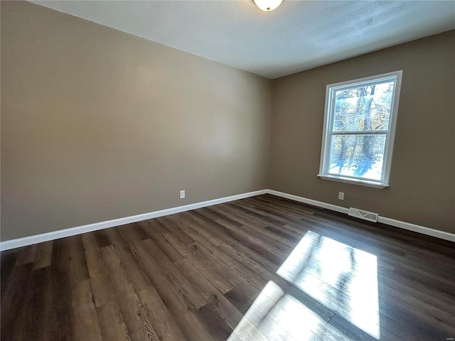 empty room featuring baseboards, visible vents, and dark wood-type flooring