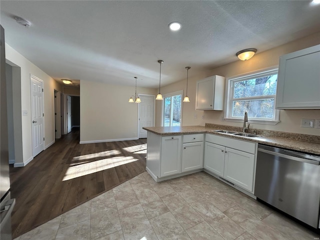 kitchen featuring pendant lighting, stainless steel dishwasher, a sink, a textured ceiling, and a peninsula