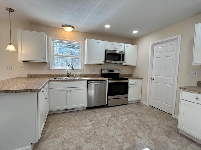 kitchen featuring appliances with stainless steel finishes, white cabinetry, a sink, and hanging light fixtures