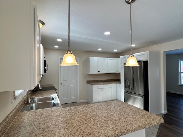 kitchen featuring a peninsula, a sink, white cabinetry, stainless steel refrigerator with ice dispenser, and pendant lighting