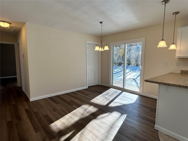 unfurnished dining area with dark wood-style flooring, baseboards, and an inviting chandelier