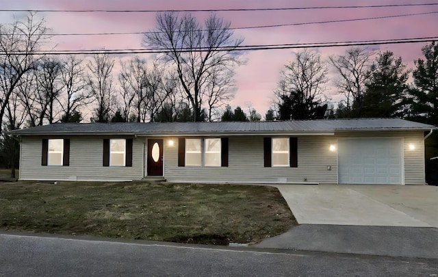 ranch-style home featuring a yard, metal roof, driveway, and an attached garage