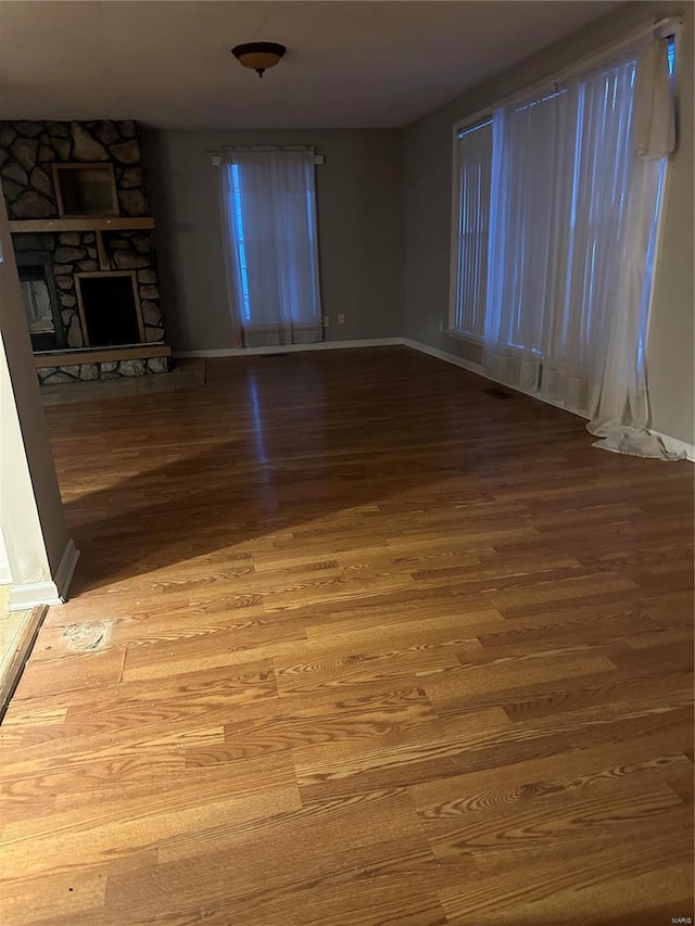 unfurnished room featuring wood-type flooring and a stone fireplace